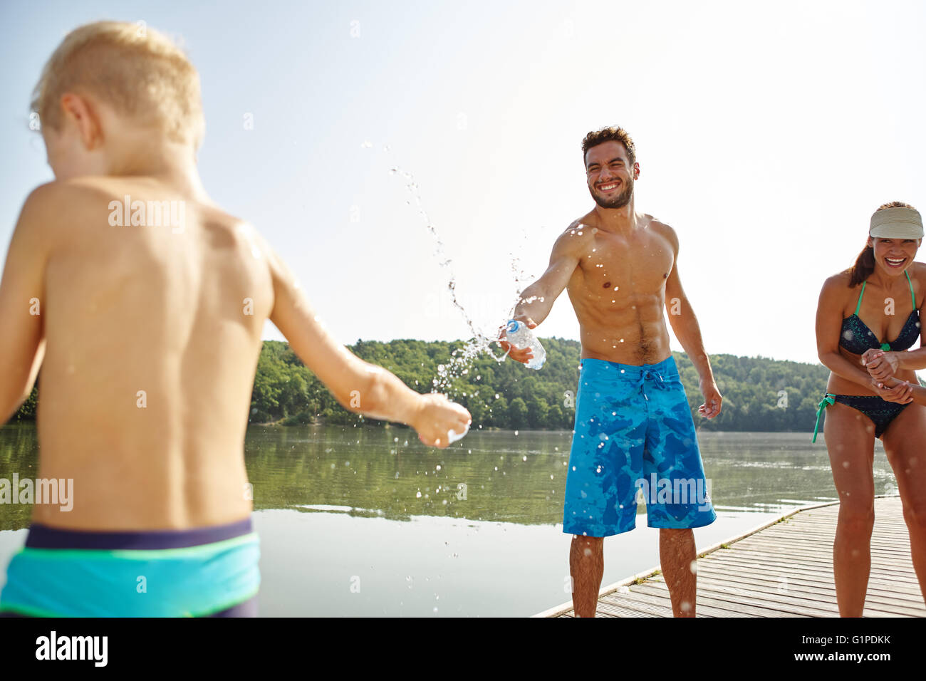 Vater und Sohn besprühen einander mit Wasser an einem See im Sommer Stockfoto