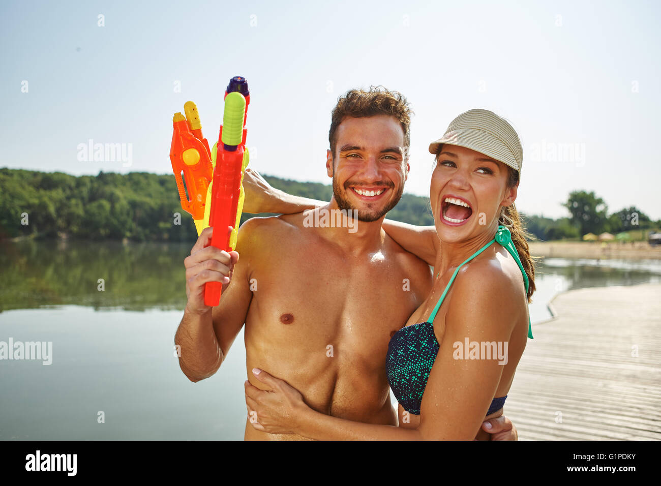 Glückliches Paar an einem See mit Spritzpistolen, Spaß haben und lachen Stockfoto