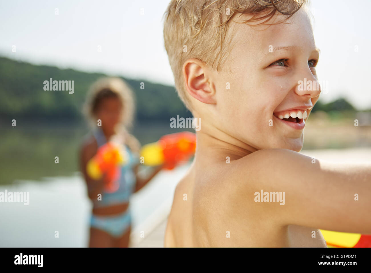 Fröhlicher Junge an einem See mit einer Wasserpistole im Sommer Stockfoto