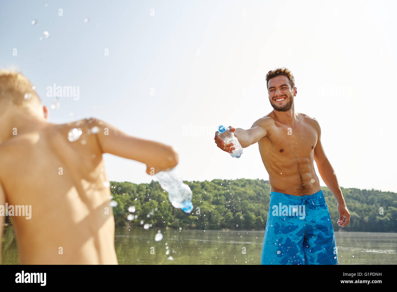 Glücklicher Vater und Sohn besprühen einander mit Wasser an einem See im Sommer Stockfoto