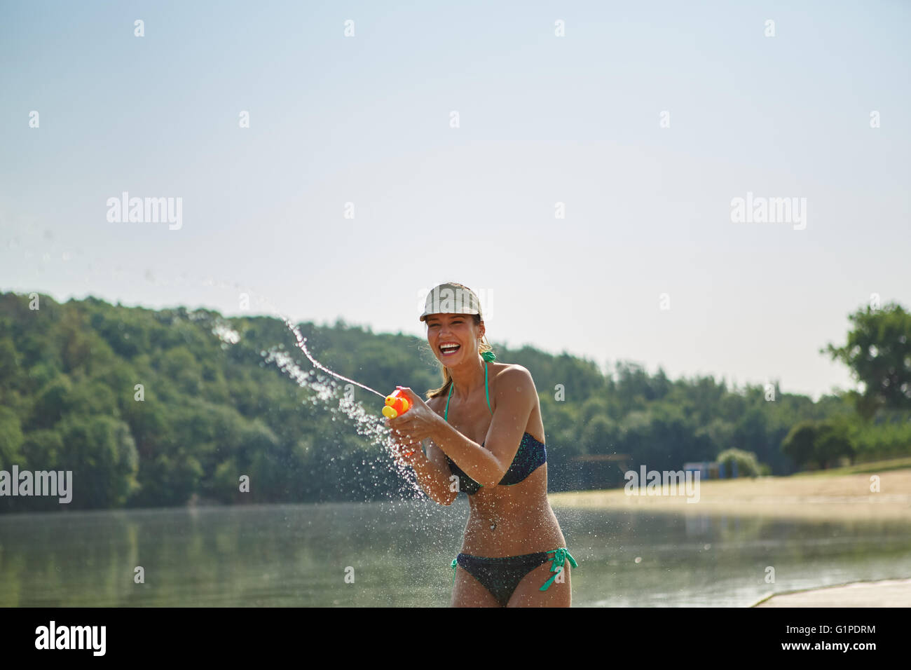 Frau an einem See Lachen und Besprühen mit einer Wasserpistole im Sommer Stockfoto