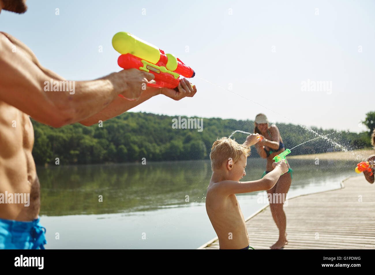 Familie an einem See Sprühwasser zueinander mit einer Spritzpistole und Spaß im Sommer Stockfoto