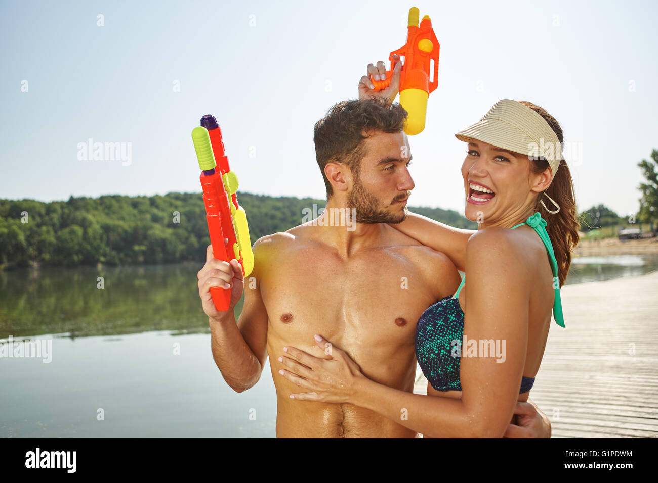 Paar an einem See mit Spritzpistolen, lachen und Spaß an Feiertagen ther Stockfoto
