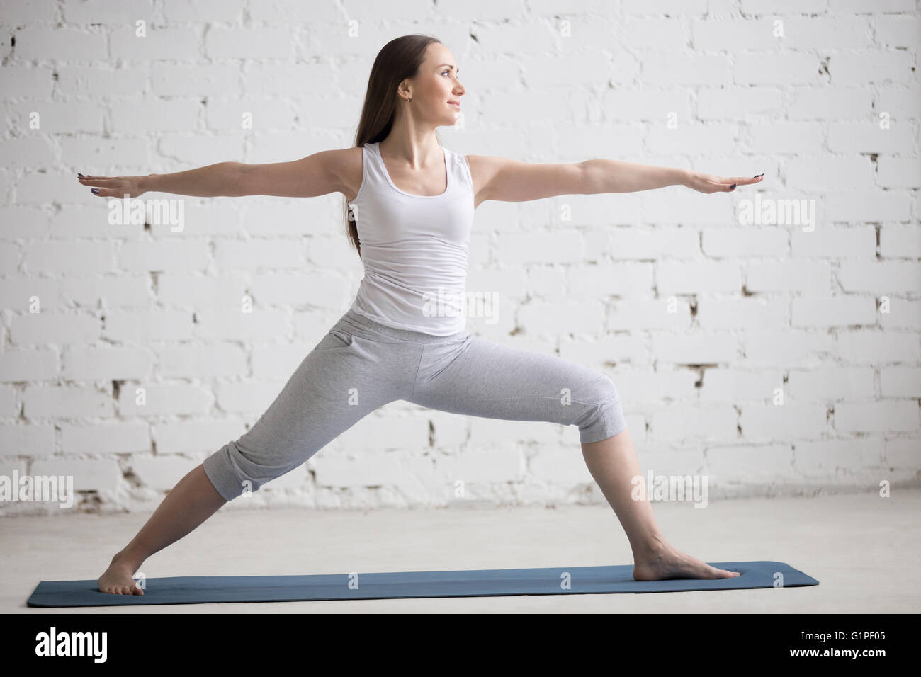 Attraktive fröhliche junge Frau drinnen trainieren. Schönes Modell Übungen auf blauen Matte im Raum mit weißen Wänden Stockfoto