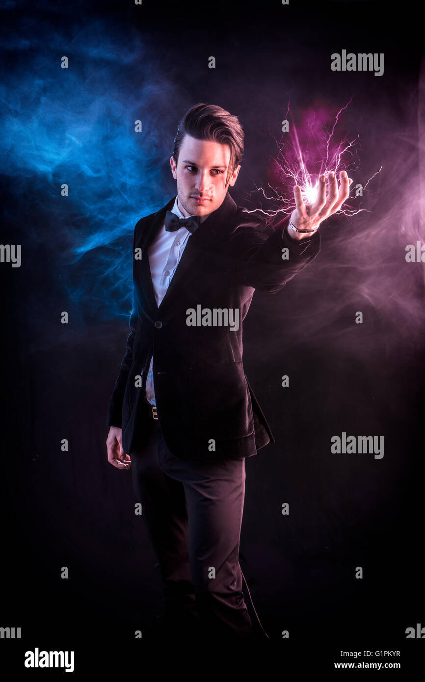 Porträt des jungen schönen Zauberer im eleganten Anzug und Fliege Blitz in der hand halten Stockfoto