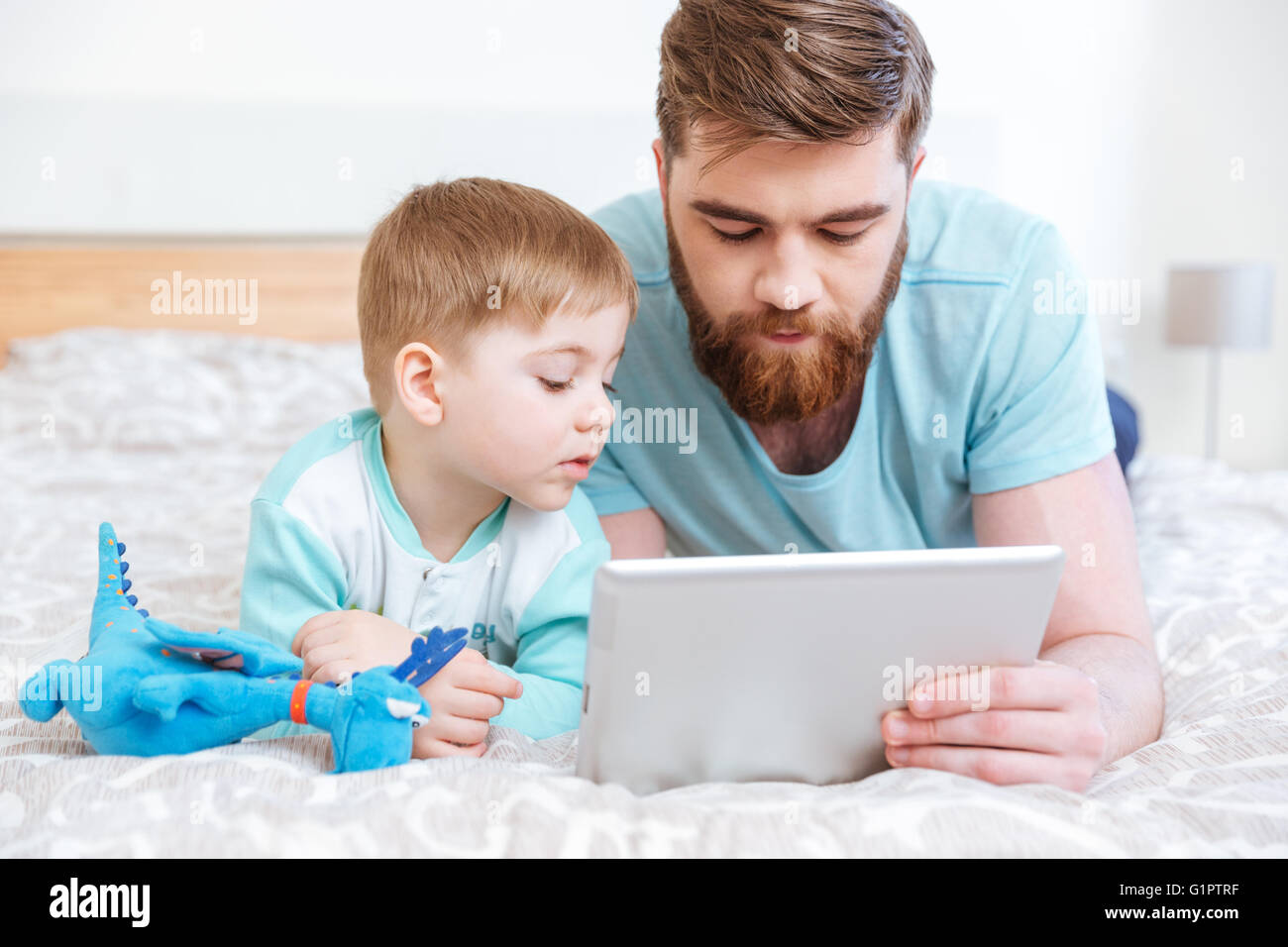 Vater und Sohn auf Bett liegend und mit Tablet zusammen zu Hause Stockfoto
