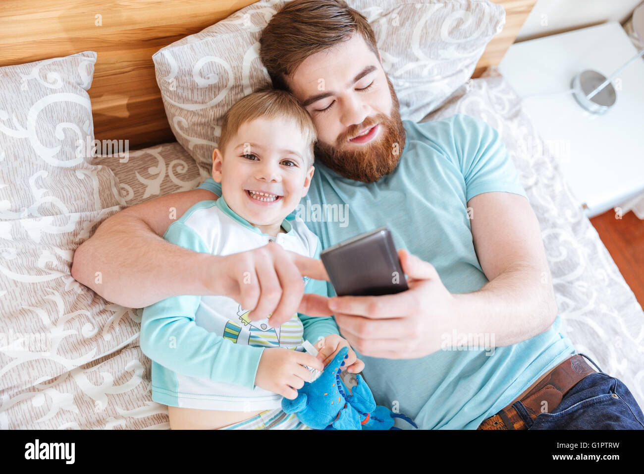 Draufsicht von Vater und Sohn auf Bett liegend und mit Handy zusammen Stockfoto