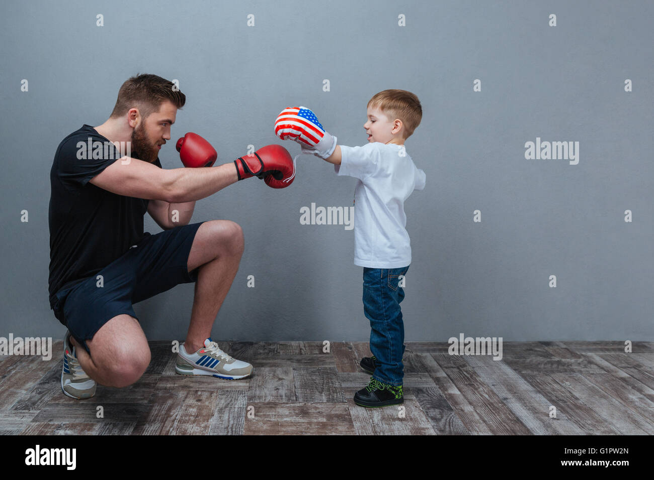 Vater und Söhnlein Training im Boxhandschuhe zusammen über grauen Hintergrund Stockfoto