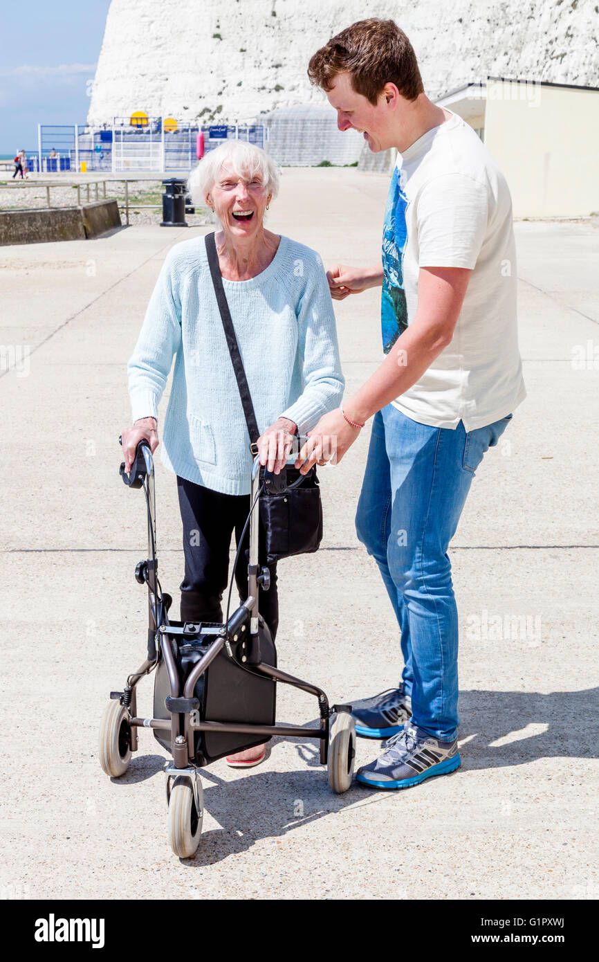 Eine ältere behinderte Frau, die mit einem Rollator Gehhilfe unterstützt durch ihren Enkel, Brighton, Sussex, UK Stockfoto