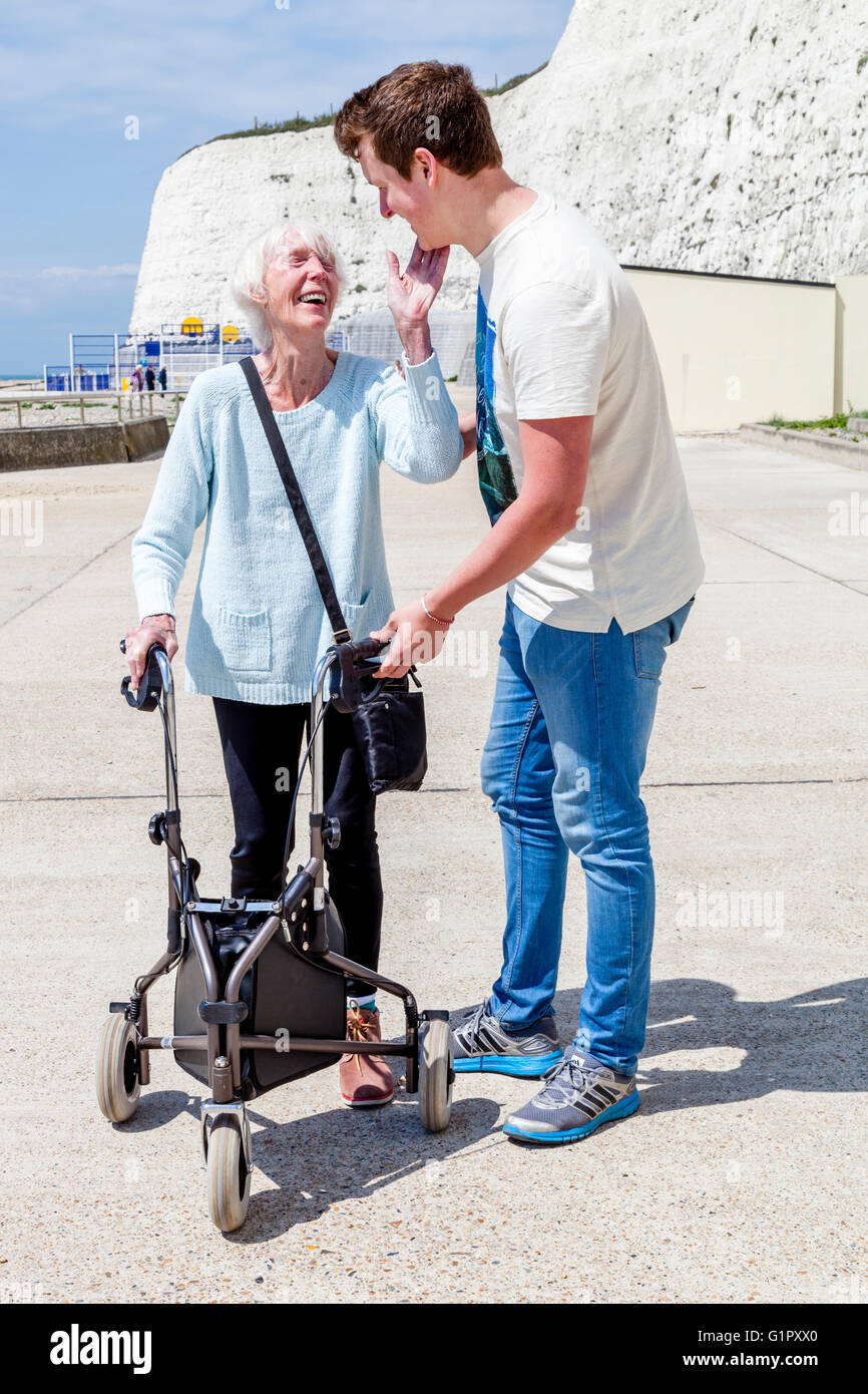 Eine ältere behinderte Frau, die mit einem Rollator Gehhilfe unterstützt durch ihren Enkel, Brighton, Sussex, UK Stockfoto
