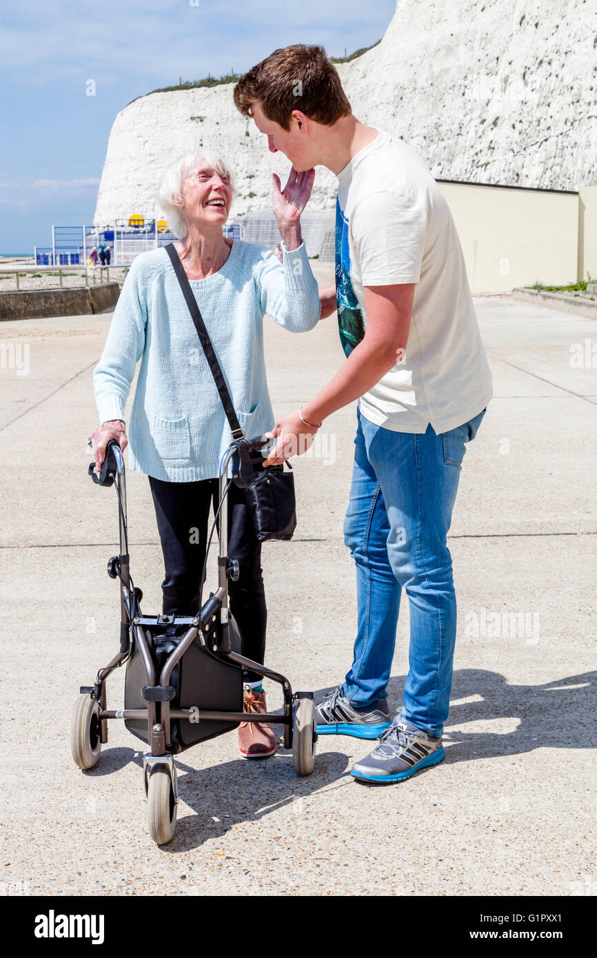 Eine ältere behinderte Frau, die mit einem Rollator Gehhilfe unterstützt durch ihren Enkel, Brighton, Sussex, UK Stockfoto