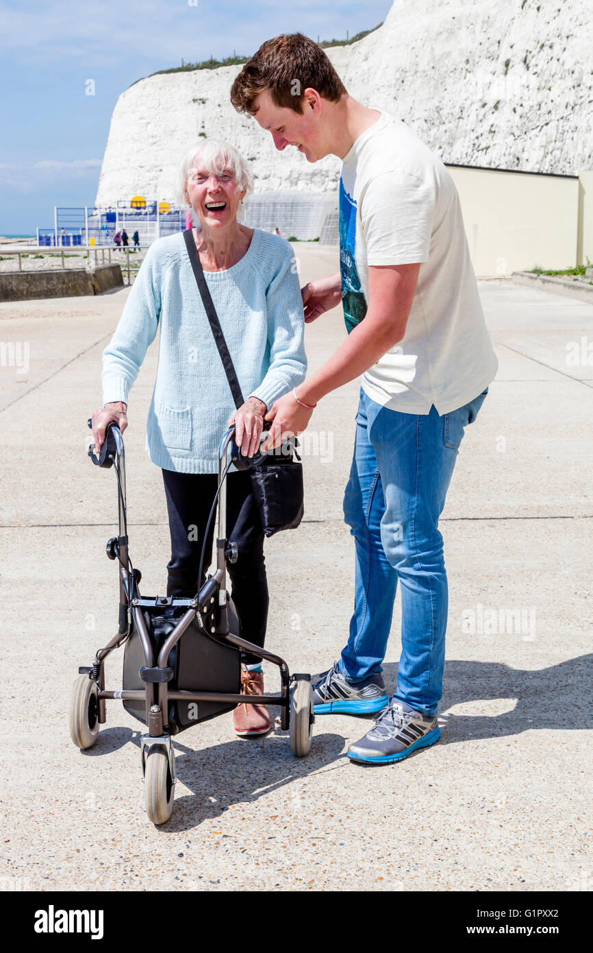 Eine ältere behinderte Frau, die mit einem Rollator Gehhilfe unterstützt durch ihren Enkel, Brighton, Sussex, UK Stockfoto
