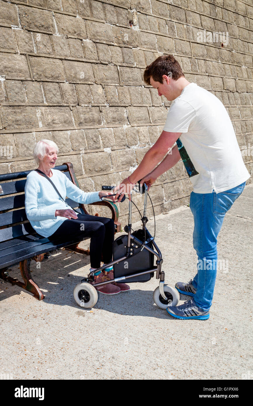 Eine ältere behinderte Frau aufstehen aus einer Bank, unterstützt durch ihren Enkel, Brighton, Sussex, UK Stockfoto