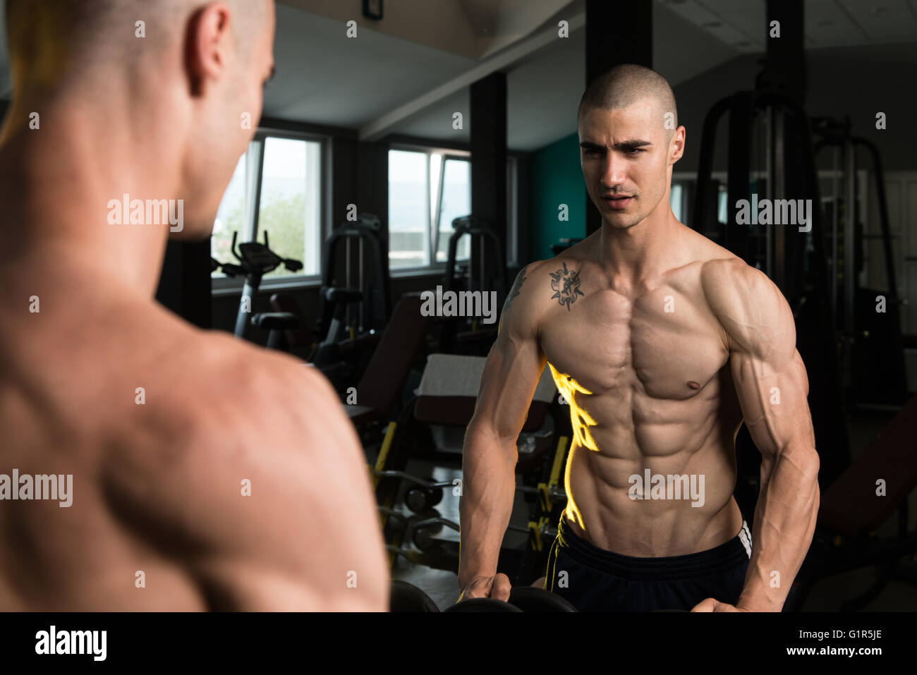 Junger Mann starke vor einem Spiegel stehen und beugen Muskeln - muskulöse athletische Bodybuilder Fitness Model posiert nach Ex Stockfoto