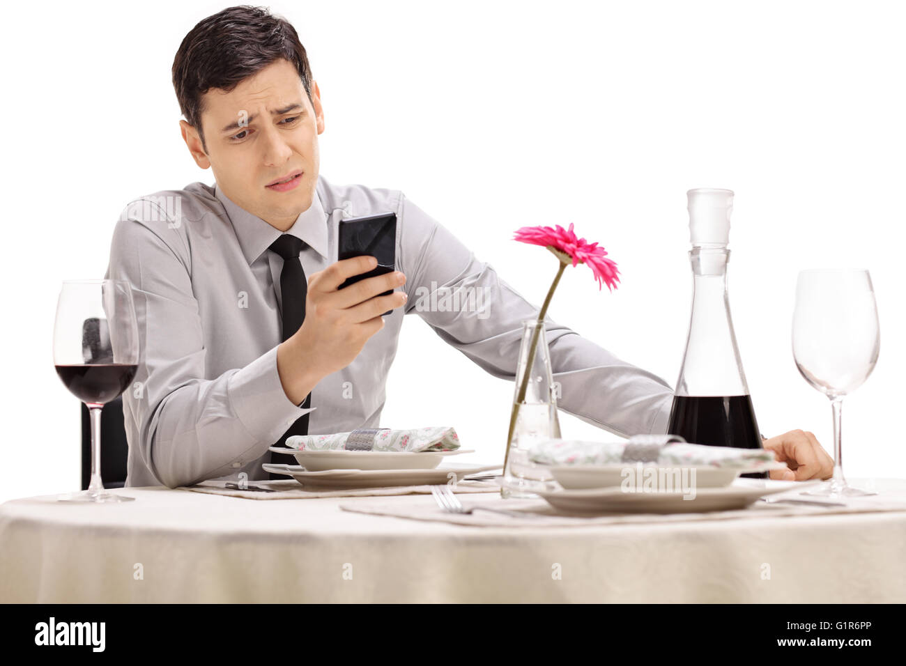 Trauriger junger Mann sitzt an einem Tisch im Restaurant und Blick auf seinem Handy isoliert auf weißem Hintergrund Stockfoto