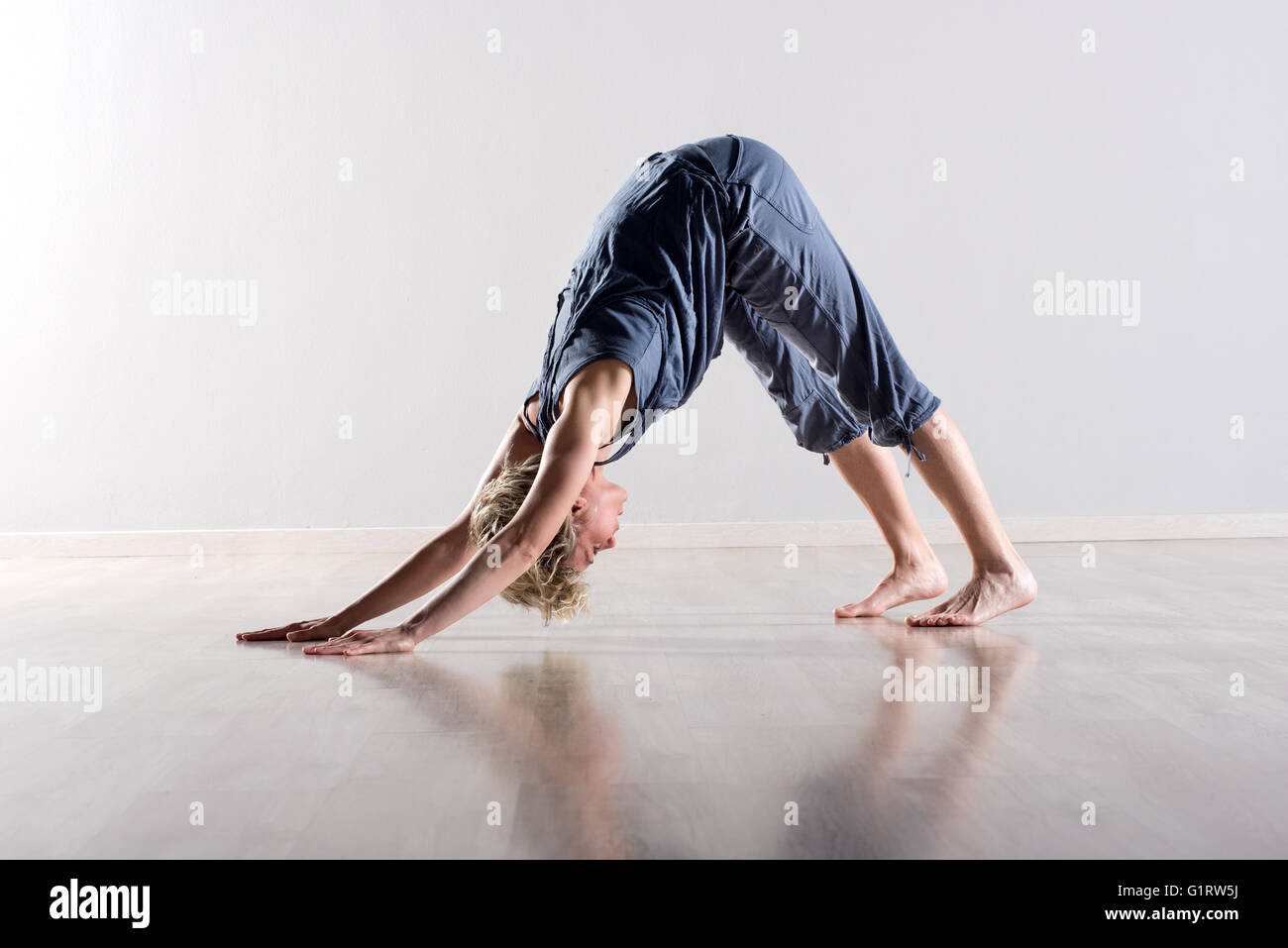 Einzelne junge kurz behaart, blonde Frau durchführen nach unten gerichteten Hund-Yoga-Pose auf Parkett Stockfoto