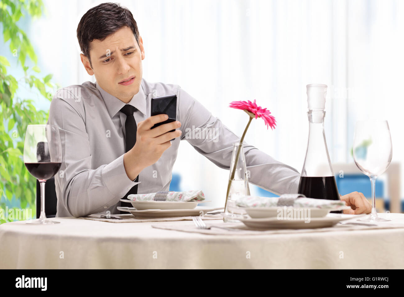 Enttäuscht junger Mann sitzt an einem Tisch im Restaurant und lesen eine SMS-Nachricht auf seinem Handy Stockfoto