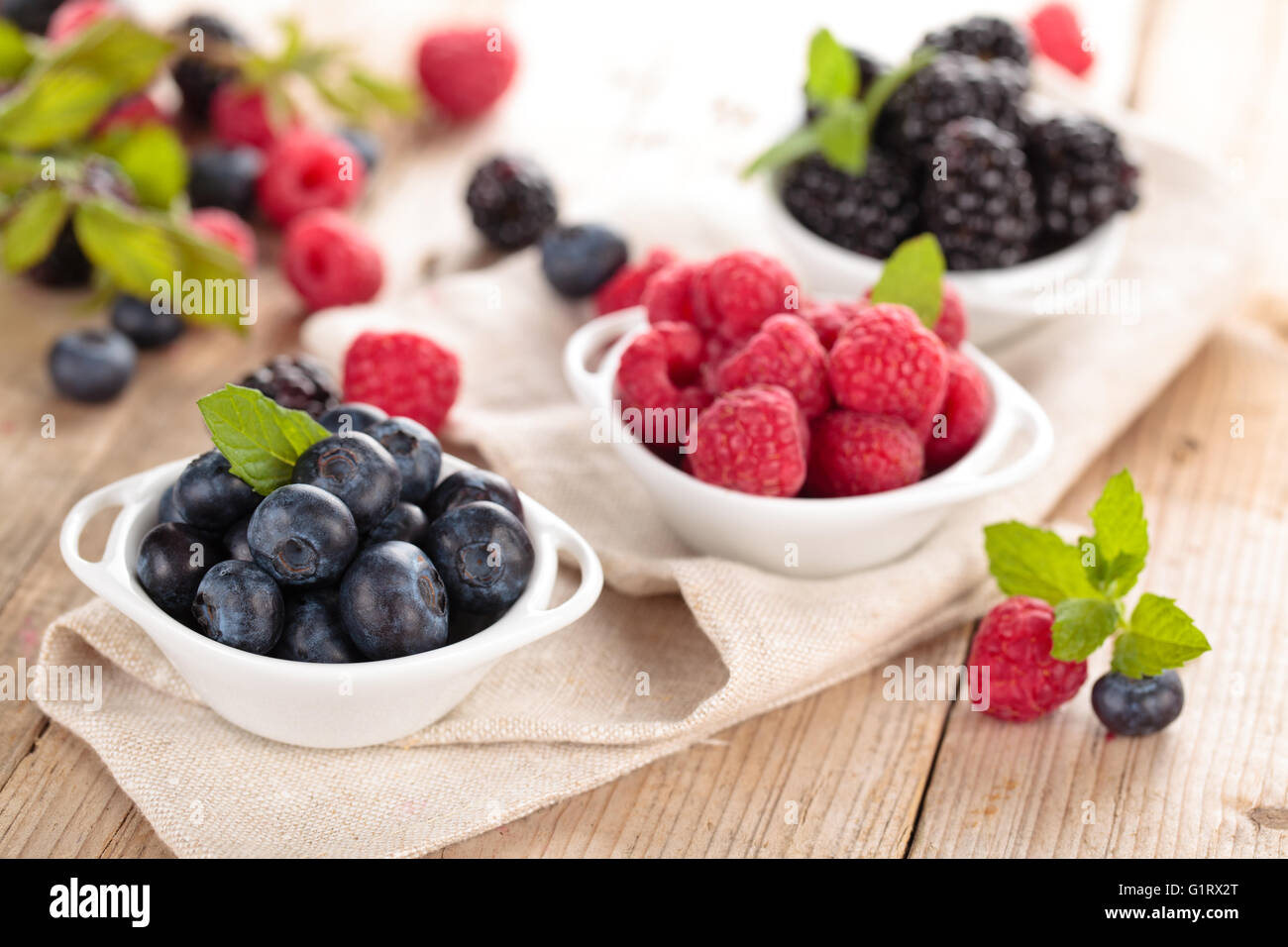 Heidelbeeren, Brombeeren und Himbeeren in kleinen weißen Schalen. Mit Minze. Auf Holztisch. Stockfoto