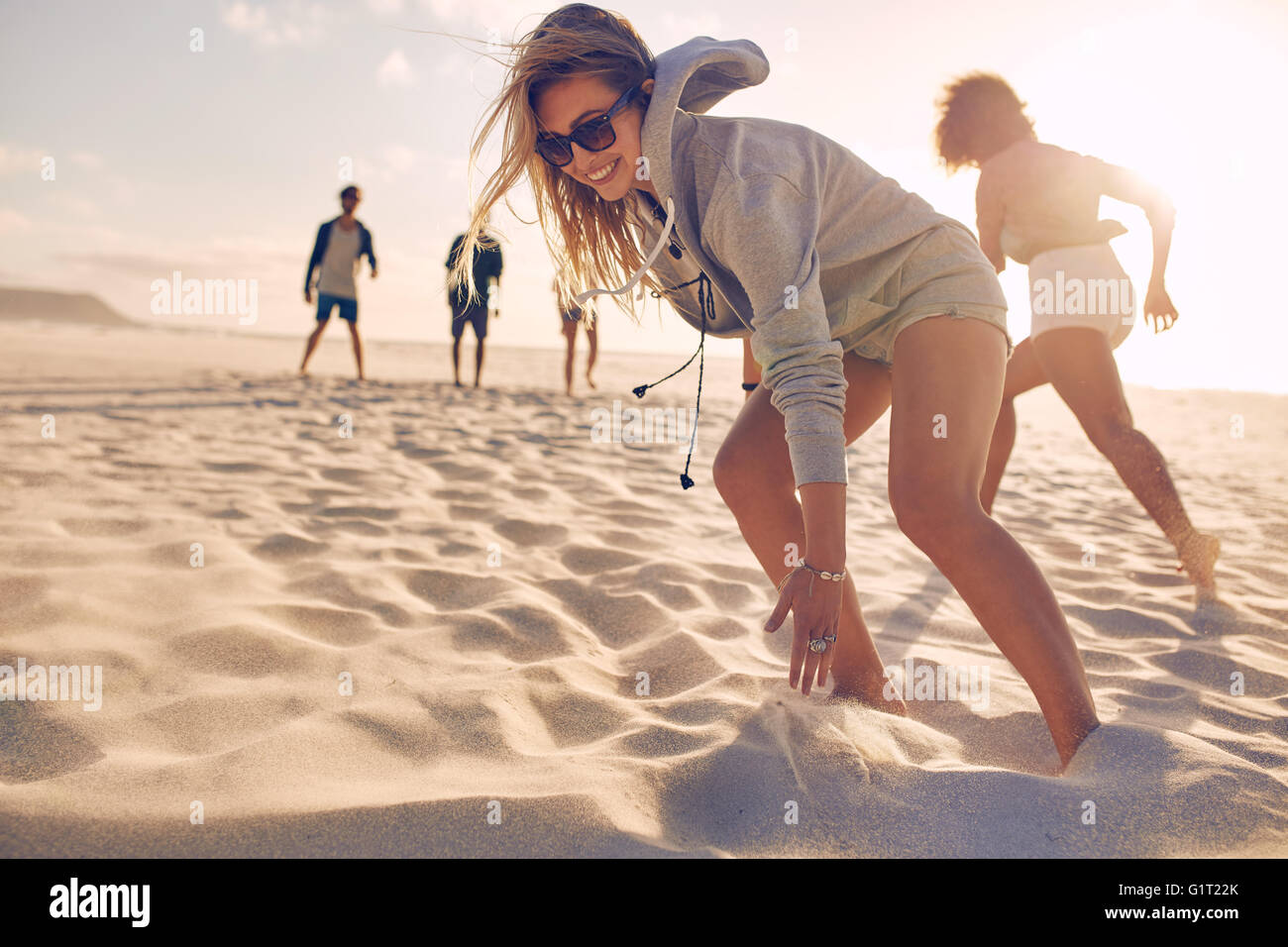 Junge Frau am Strand mit Freunden Rennen. Gruppe von Jugendlichen, die an einem Sommertag am Sandstrand spielen. Stockfoto