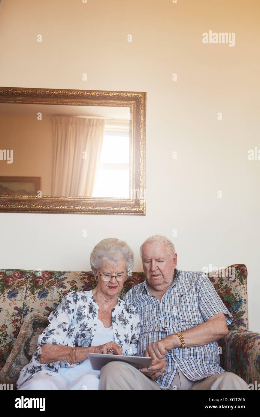 Vertikale Innenaufnahme des Ehepaar im Ruhestand mittels zu Hause digital-Tablette. Senior kaukasischen Mann und Frau sitzen zusammen auf sofa Stockfoto