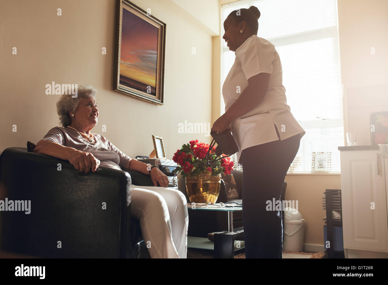 Ältere Frau sitzend auf einem Stuhl zu Hause mit weiblichen Betreuer stehen. Krankenschwester visiting senior Patienten zur Überprüfung blo Stockfoto