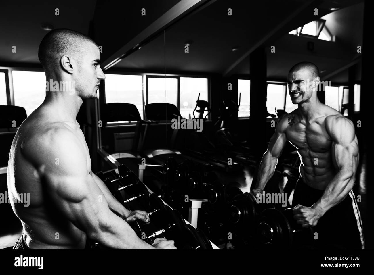 Junger Mann starke vor einem Spiegel stehen und beugen Muskeln - muskulöse athletische Bodybuilder Fitness Model posiert nach Ex Stockfoto
