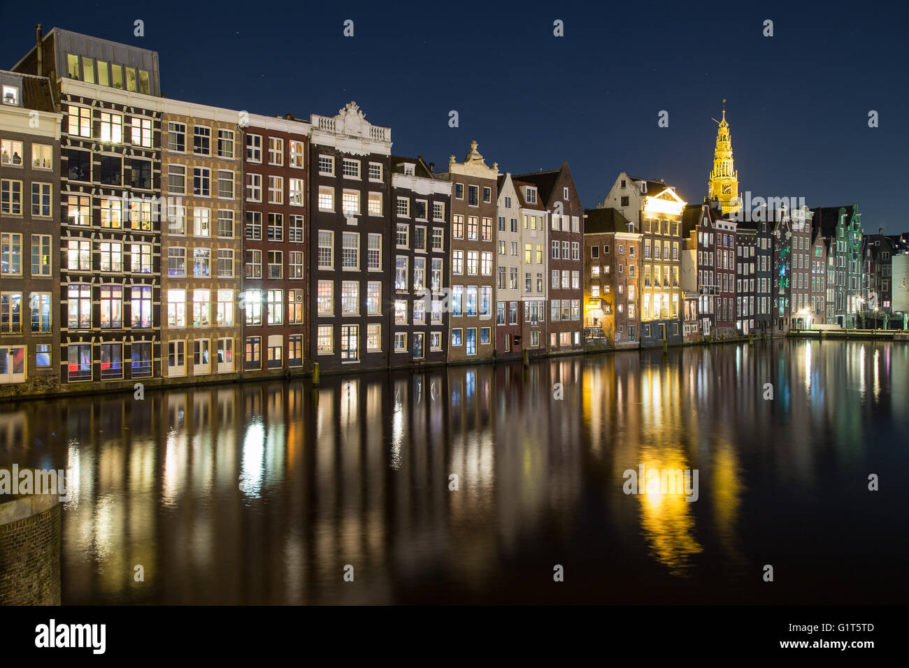 Alte Gebäude entlang der Damrak in Amsterdam bei Nacht. Reflexionen im Wasser zu sehen. Stockfoto
