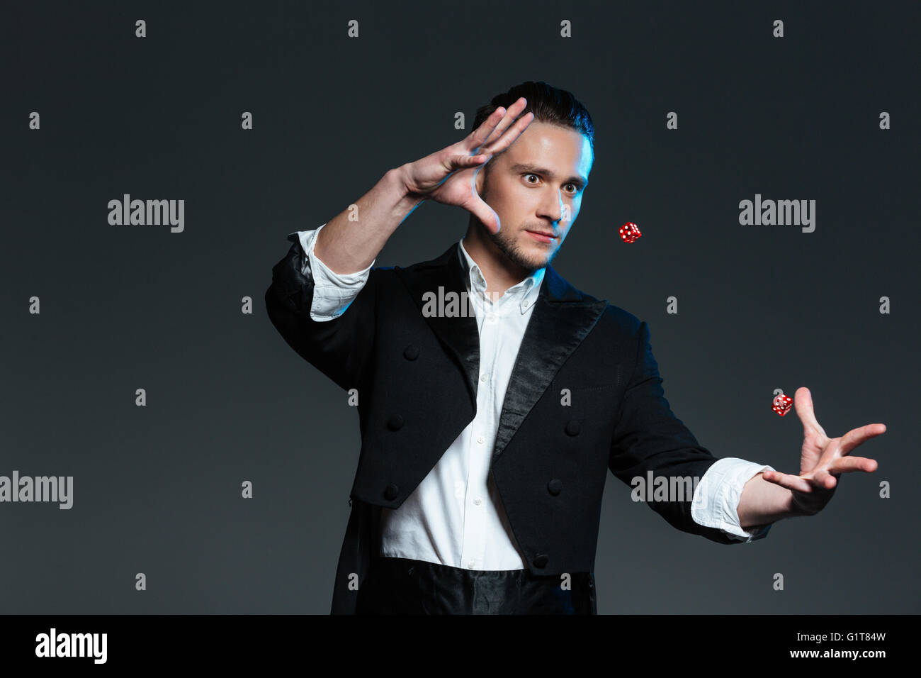 Hübscher junger Mann Magier zeigt Tricks mit grauem Hintergrund Würfel überfliegen Stockfoto