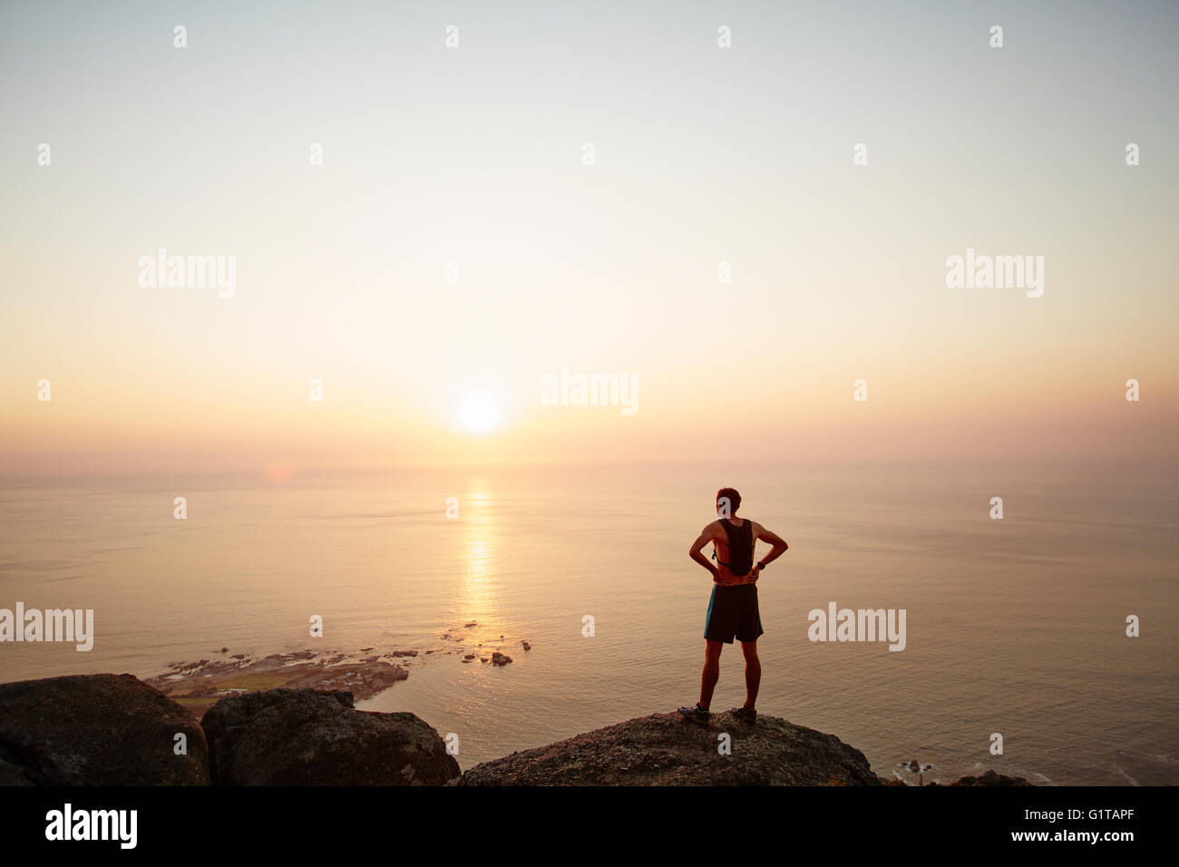 Männliche Läufer auf Felsen, Blick auf den Sonnenuntergang mit Meerblick Stockfoto