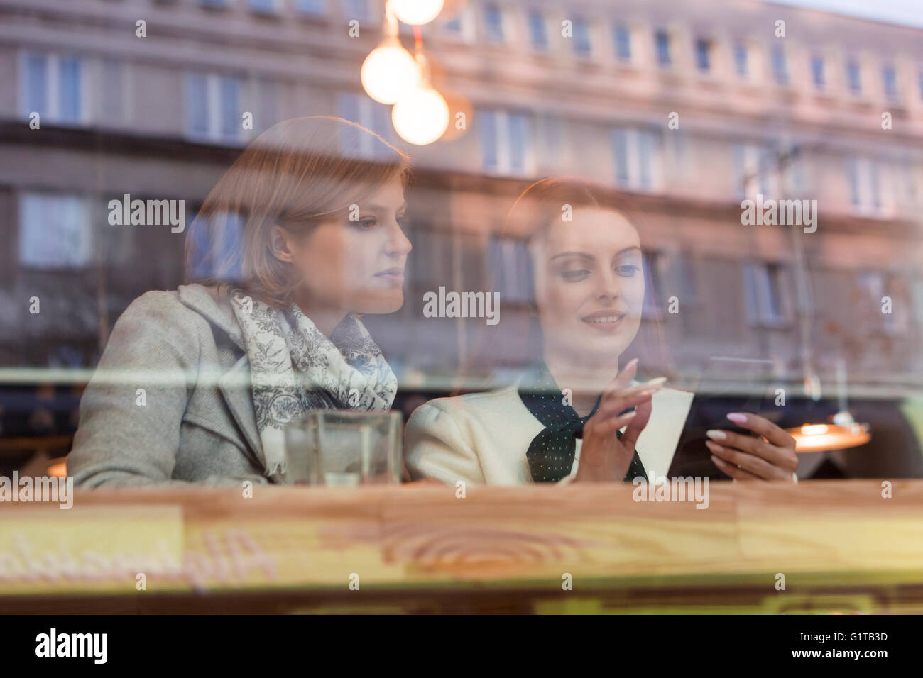 Unternehmerinnen mit Handy am Café Fenster Stockfoto