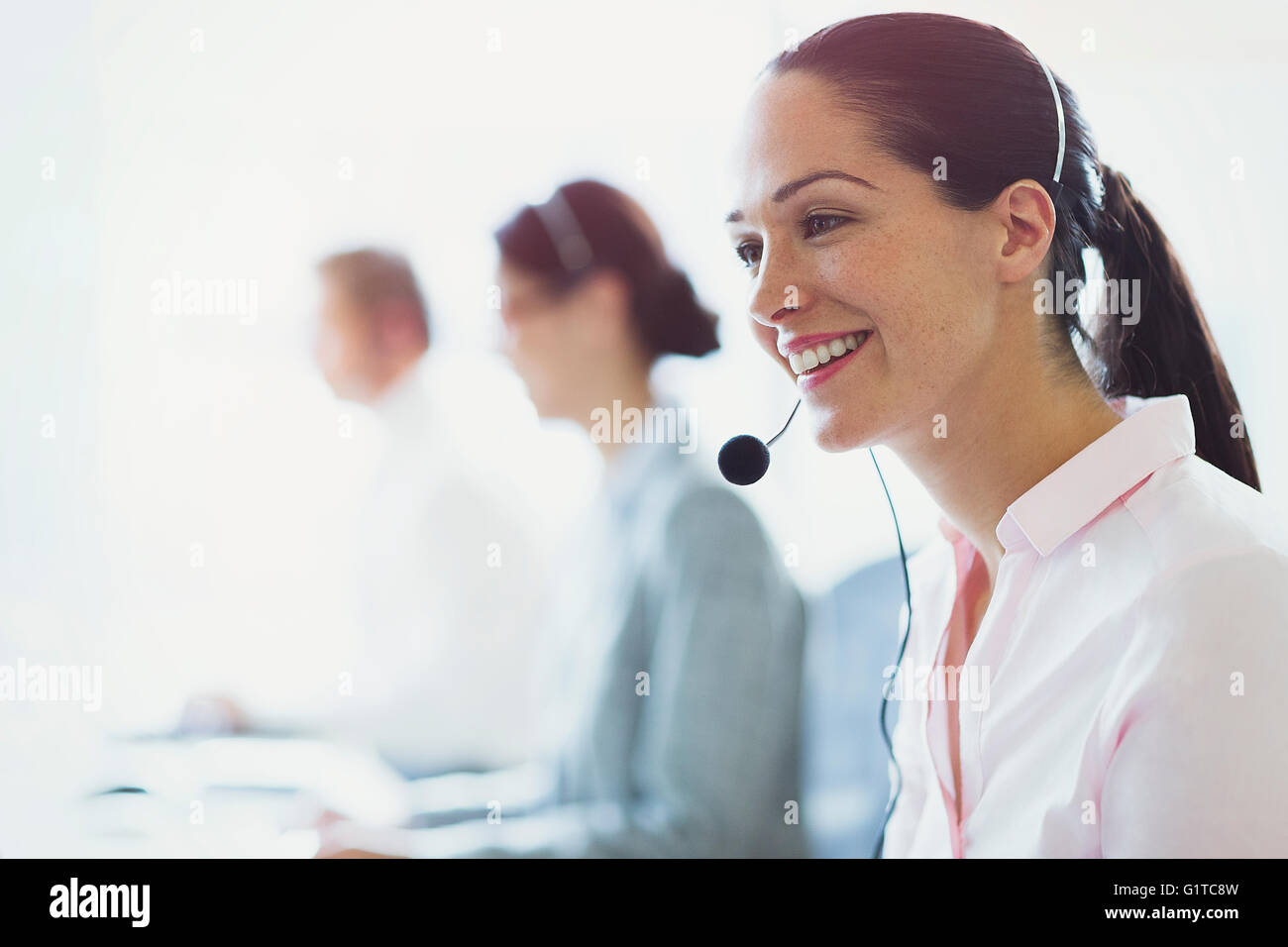 Lächelnde Geschäftsfrau im Gespräch am Telefon mit Kopfhörer Stockfoto