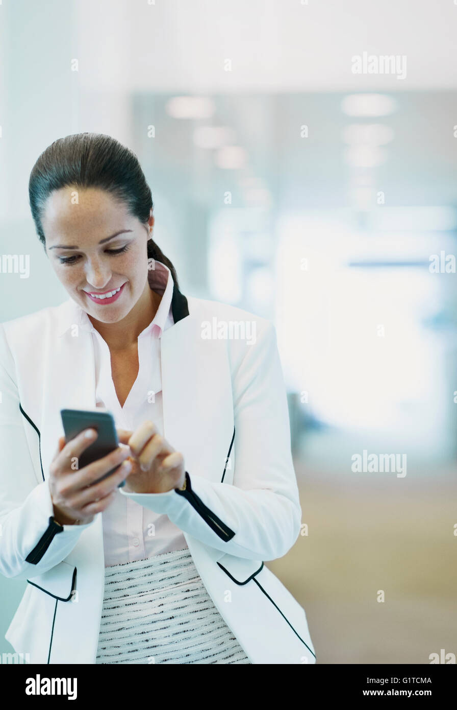 Lächelnde Geschäftsfrau mit Handy im Büro Korridor Stockfoto