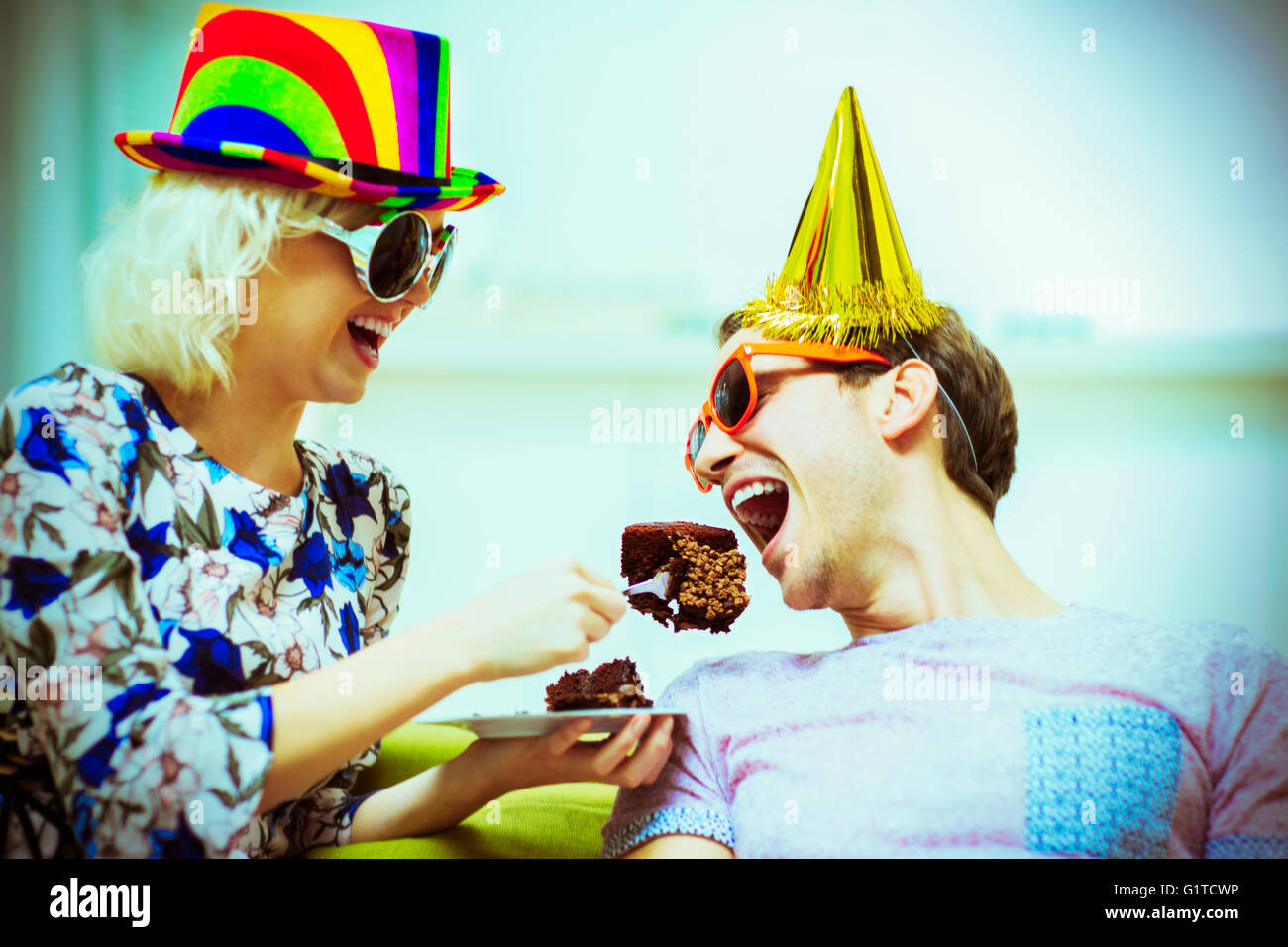 Verspielte Paar Partyhüte und Sonnenbrillen essen Schokolade Kuchen Stockfoto