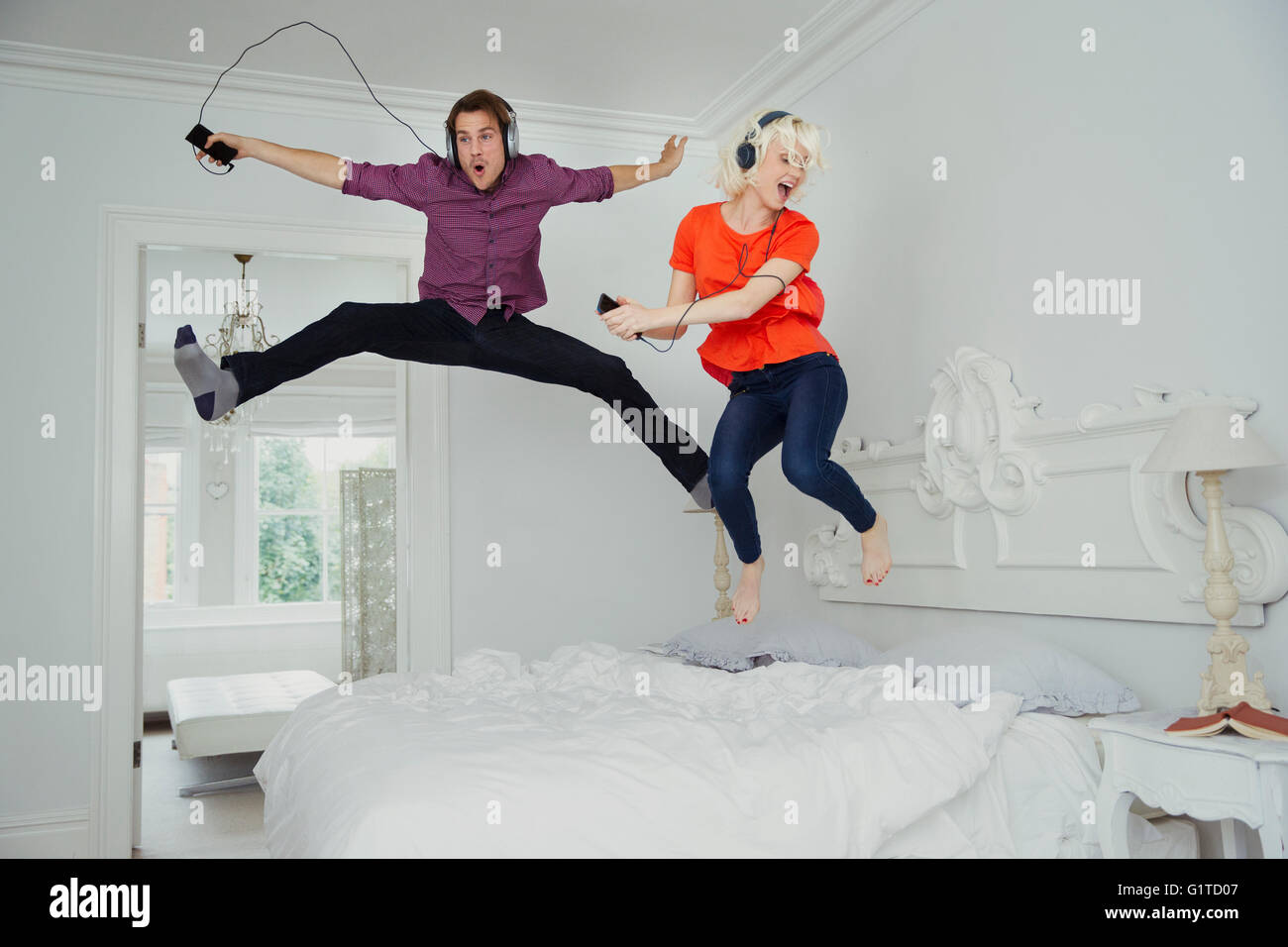 Verspieltes paar springen auf Bett und Musikhören mit MP3-Player und Kopfhörer Stockfoto