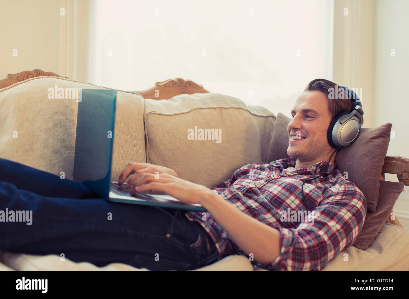 Mann mit Kopfhörer mit Laptop auf dem Sofa im Wohnzimmer Stockfoto
