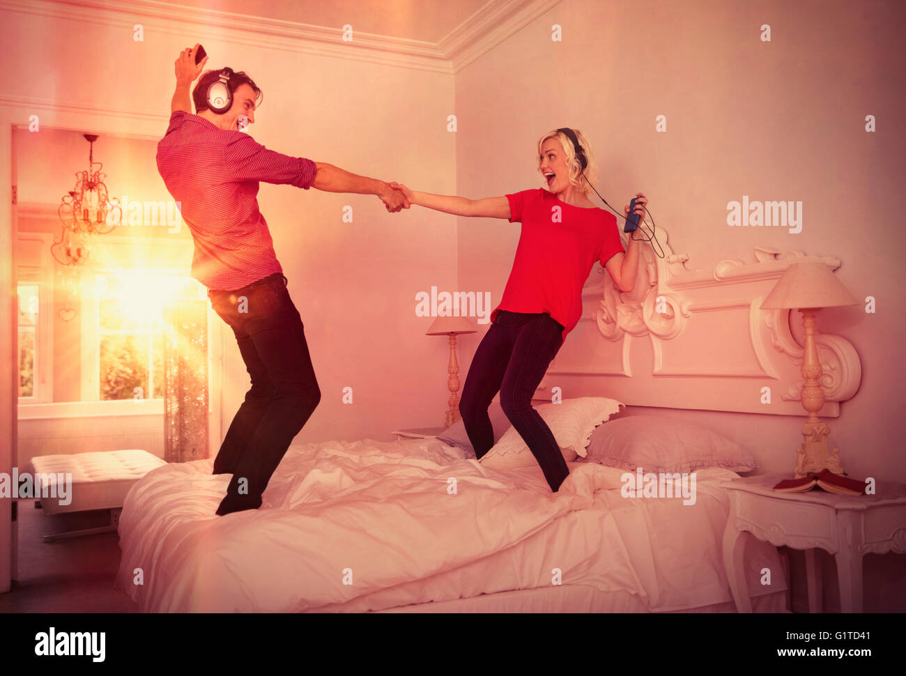 Verspielte Paare tanzen auf Bett Musikhören mit MP3-Player und Kopfhörer Stockfoto