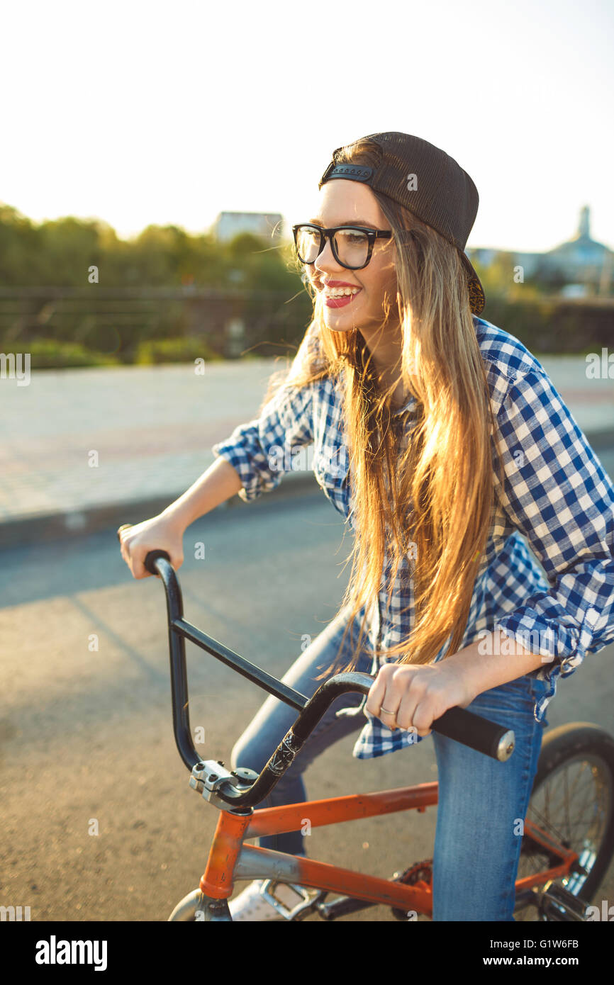 Schöne junge Frau mit Hut mit dem Fahrrad auf Stadt Hintergrund im Sonnenlicht im Freien. Aktive Menschen Stockfoto