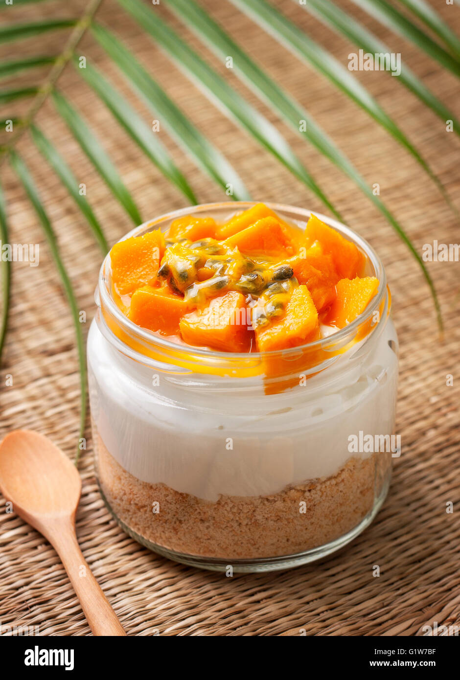 Käsekuchen im Glas mit tropischen Früchten: Mango, Passionsfrucht auf Stroh Hintergrund Stockfoto