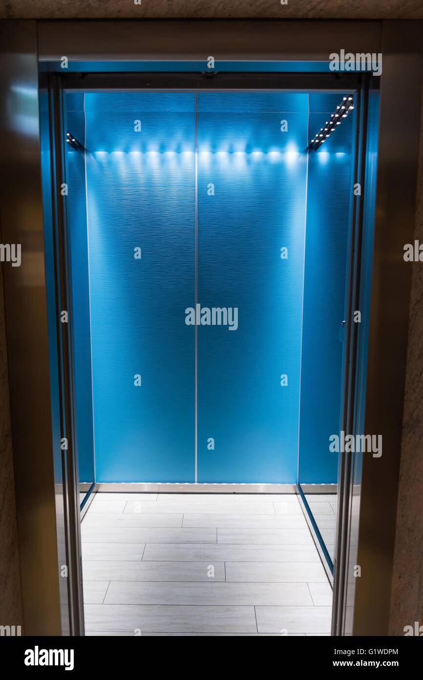 Eine leere blaue Aufzug oder Lift mit Metalltüren, die in Gebäude mit Beleuchtung offenstehen. Vertikale Foto Stockfoto