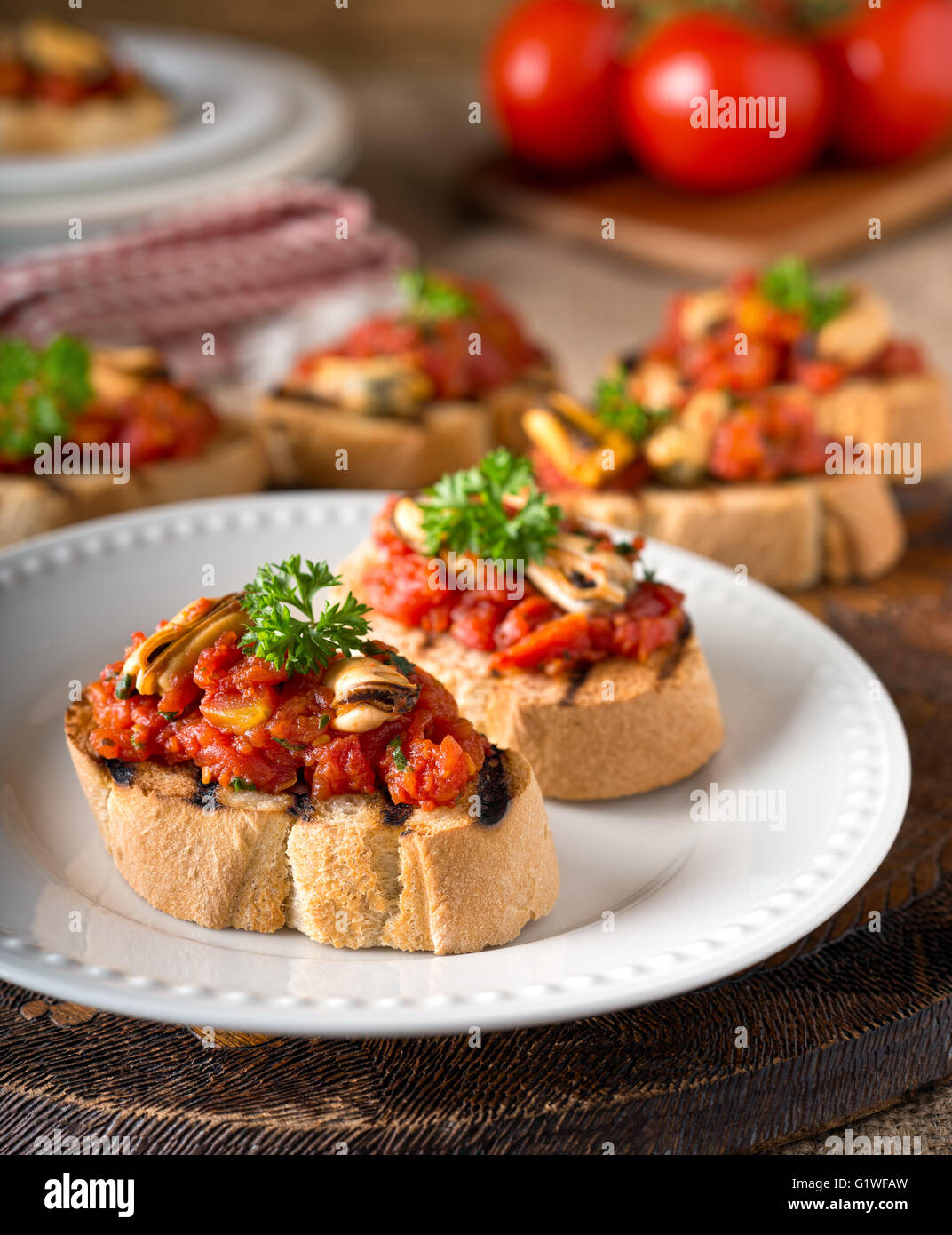 Leckere Muscheln Bruschetta mit Tomaten, Petersilie, Olivenöl und Knoblauch auf gegrilltes Baguette. Stockfoto