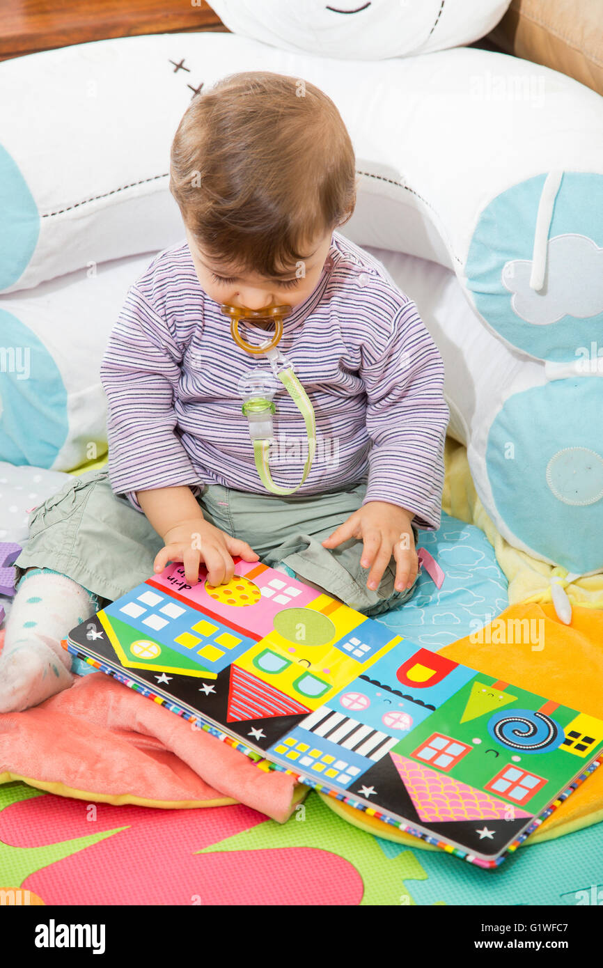 Einjähriges Baby sitzen auf Boden und leuchtend buntes Buch mit Bildern zu betrachten Stockfoto