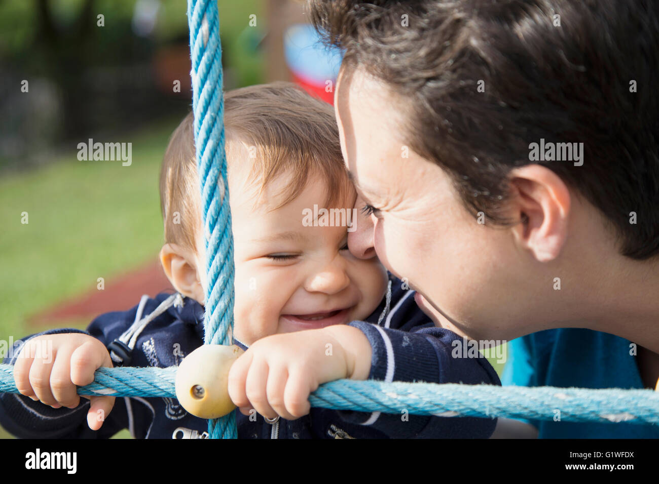 Nahaufnahme von schwarzhaarige Mutter und lächelnd ein Jahr altes Baby, Hand in Hand auf blaues Seil Stockfoto