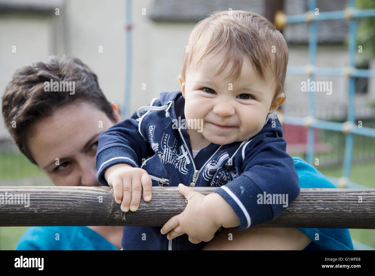 Mutter hält eines Jahres altes Baby während sie hängen Holzbar und lächelt in die Kamera mit lustigem Gesicht Stockfoto