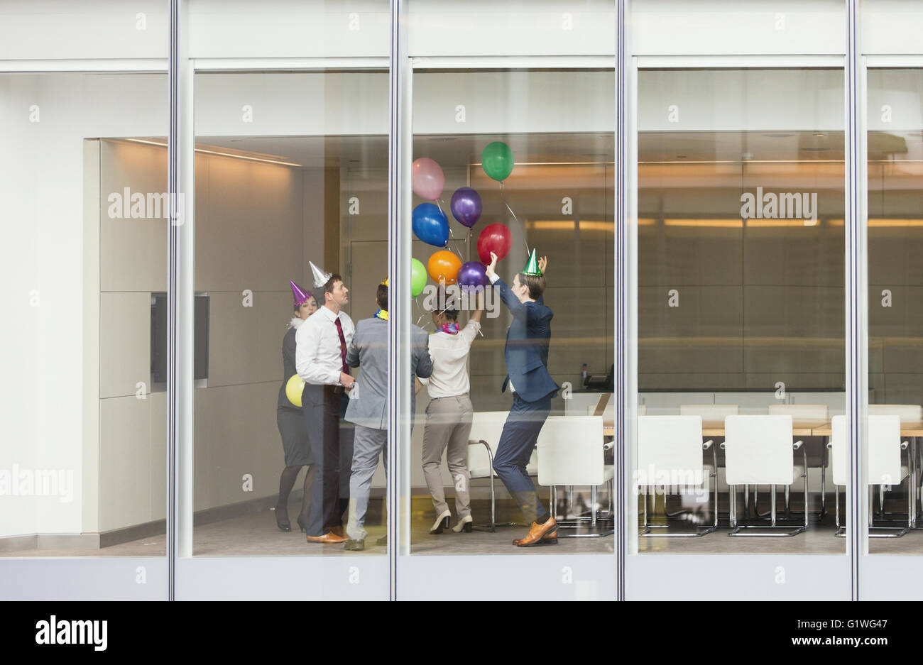 Spielerische Geschäftsleute in Partyhüte feiern mit Luftballons im Konferenzraum Stockfoto