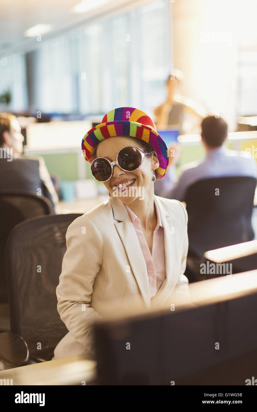 Porträt von lächelnden Geschäftsfrau in alberne Sonnenbrille und gestreiften Hut arbeiten im Büro Stockfoto