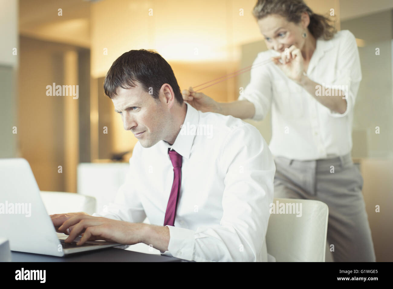 Schelmischen Geschäftsfrau mit dem Ziel Gummiband an ahnungslose Geschäftsmann arbeiten am laptop Stockfoto