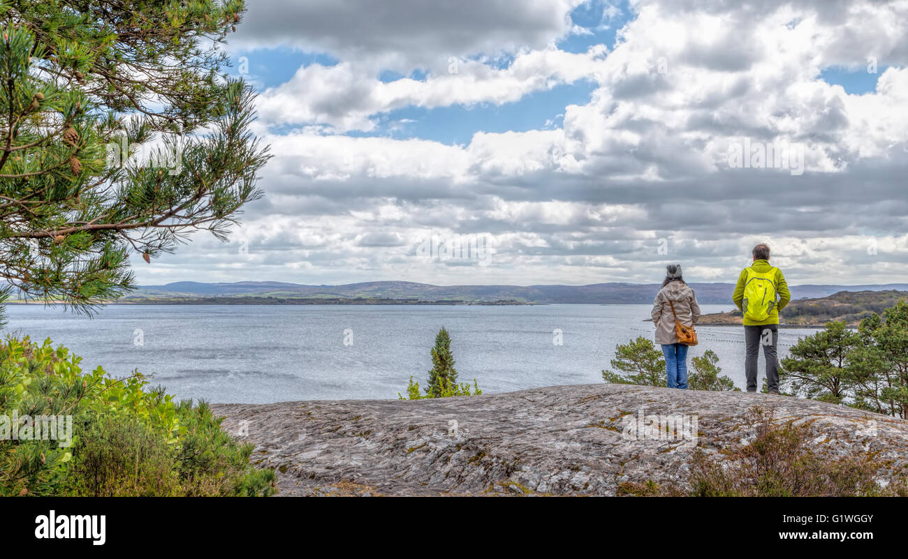 Menschen Sie stehen auf einer Klippe & genießen Sie die Aussicht auf die Bantry Bay aus Garnish Island oder Ilnaculin, Beara Halbinsel, Co. Cork, Irland. Stockfoto