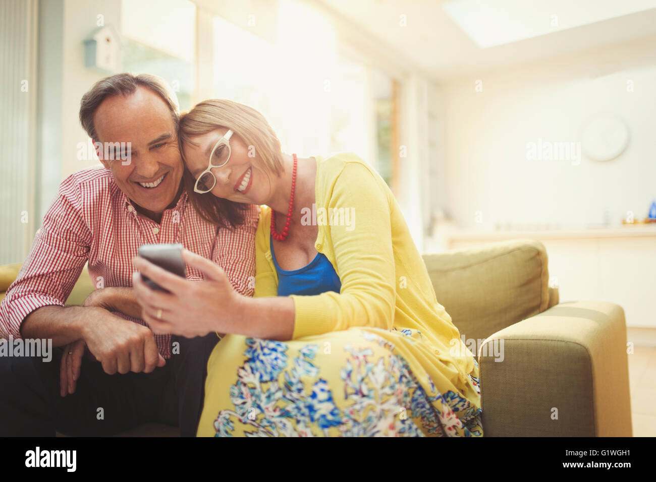 Lächelnd älteres paar SMS mit Handy im Wohnzimmer Stockfoto