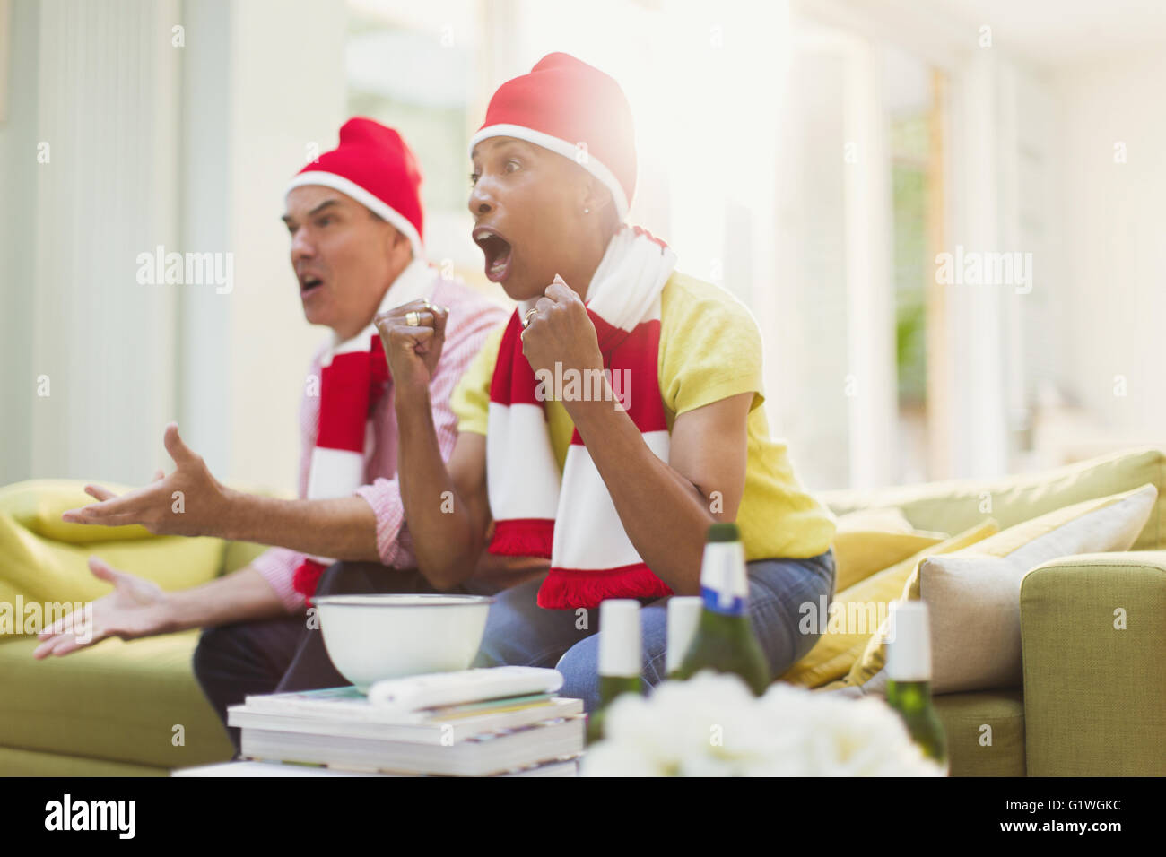 Älteres Paar tragen passende Hüte und beobachten TV-Sport-Event im Wohnzimmer jubeln Stockfoto