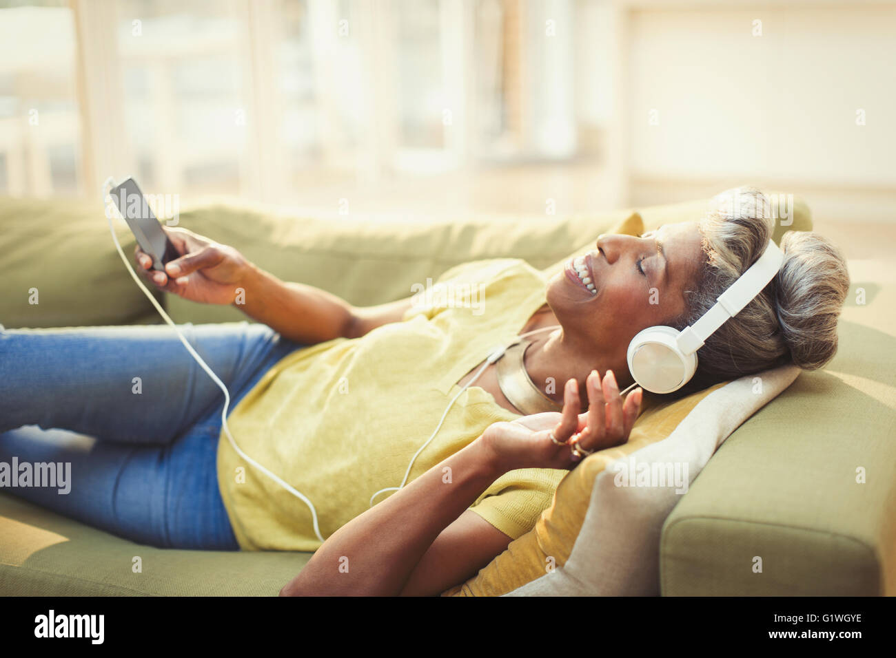 Komfortable Reife Frau Musikhören mit Kopfhörer und MP3-Player im Wohnzimmer-sofa Stockfoto